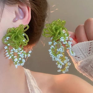 Detail of beaded flower earrings with green leaf clusters and white dangling tassels