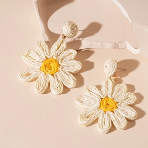 Close-up of hand-woven white daisy earrings with yellow centers and silver pins