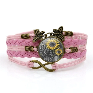 Detail of multi-layer pink leather bracelet with sunflower glass gem and butterfly charms