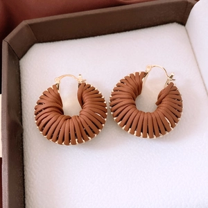 Détail de boucles d'oreilles circulaires en cuir tressé marron café avec cadre doré