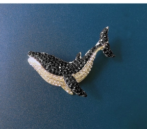 Macro shot of a sparkling whale brooch with black and white rhinestones on blue background
