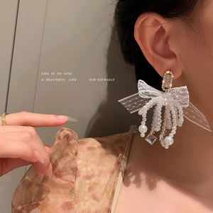 Elegant bow earrings with white lace, pearls, and crystals on a side-view model