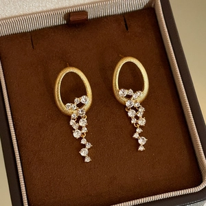 Élégantes boucles d'oreilles ovales dorées avec cristaux dans une boîte à bijoux