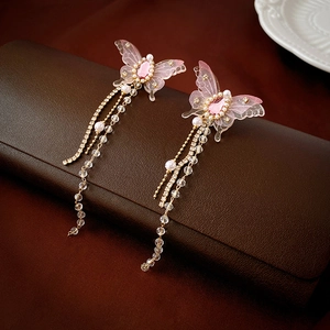 Pink butterfly tassel drop earrings with crystals and pearls on leather surface