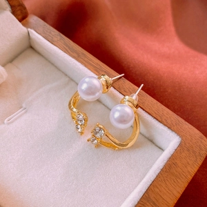 Detailed close-up of C-shaped gold earrings with pearls and crystals in a velvet jewelry box