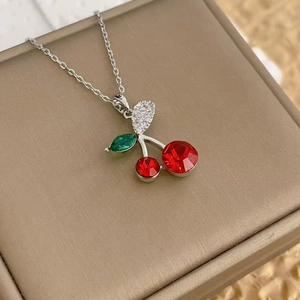 Close-up of a silver cherry pendant necklace with red and green crystals on a gift box