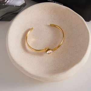 Macro view of gold plated stainless steel open bangle with oval cubic zirconia on tray