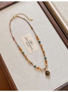 Collier de perles rétro avec breloques en verre et détails dorés sur tissu beige