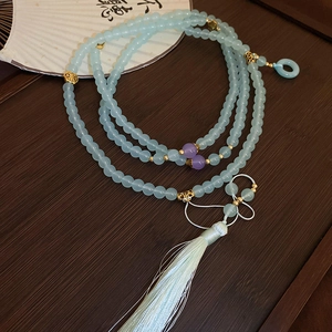 Detailed close-up of light blue glass beads with a tassel and a jade-like donut pendant