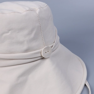 Detail of light beige wide-brim sun hat showing textured fabric and pearl button