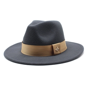 Detail of grey wool fedora hat featuring a brown ribbon and a golden bee metal logo
