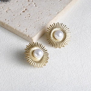 Golden sunburst stud earrings with white pearls on a minimalist stone background
