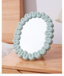 Detail of light green wavy frame desktop mirror on a cozy wooden bedside table