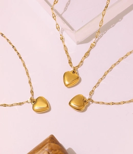 Detailed view of three gold heart pendant necklaces on soft pink display