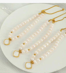 Detail of three pearl bracelets with golden shell charms on a white ceramic plate
