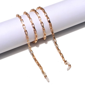 Detailed view of golden square link eyewear chain with diamond texture on white stand