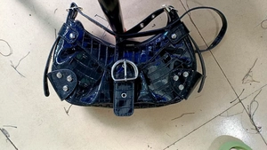 Detail of crocodile embossed faux leather handbag with metallic rivets and D-ring buckle