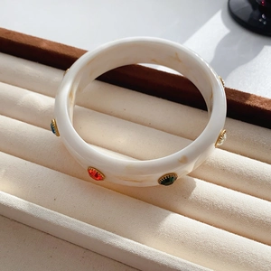 Detail of cream acrylic resin bangle with colorful rhinestones on a jewelry tray