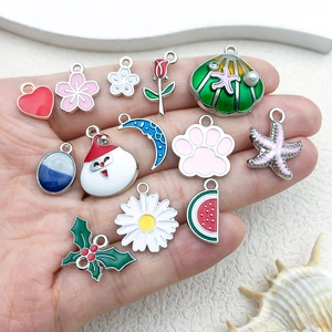 Various enamel alloy charms including heart and starfish held in palm for size display