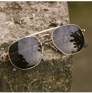Detailed outdoor shot of gold pilot sunglasses with grey lenses on a grey stone surface
