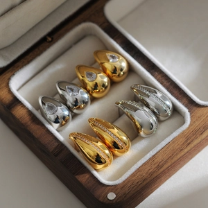 Detail of gold and silver teardrop earrings with zircons in a dark wood jewelry box