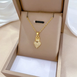 Close-up of a gold crown heart necklace with sparkling crystals in a beige jewelry box