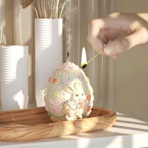 Detail of lit Easter egg candle featuring rabbit relief and colorful Celebrate text