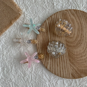 Starfish and seashell hair clips with pearls and glitter on a wooden background