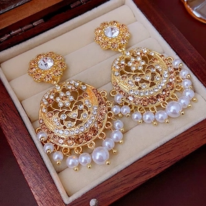 Vintage gold-tone chandelier earrings with pearls and crystals on a beige velvet display