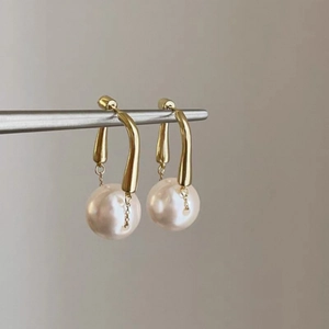 Detailed close-up of elegant gold curved metal drop earrings with large round white pearls