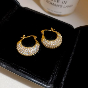Macro shot of gold-plated U-shaped earrings with pave-set zircons on black velvet box