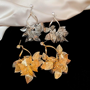 Detailed view of gold and silver hollow leaf drop earrings on silk and velvet background