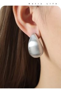Close-up of a large silver teardrop earring with a matte finish on a model's ear