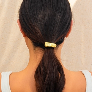 Close-up of a glossy gold geometric metal hair tie on a model with a low ponytail