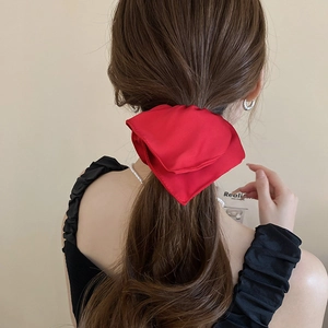 Rear view of a model wearing a red satin bow hair tie on a neat ponytail hairstyle