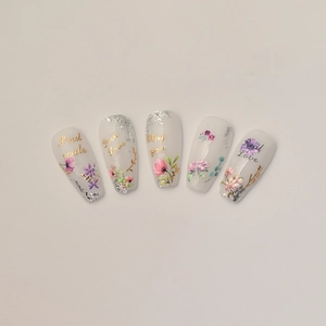 Detail of coffin shape press-on nails with floral patterns, gold foil and romantic text