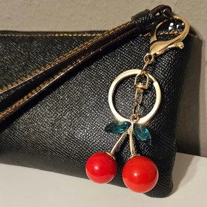 Close-up of a 3D red cherry keychain with green crystal leaves on black leather bag
