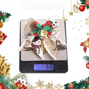 Detailed view of handmade linen snowman Christmas bow with a golden bell on a digital scale
