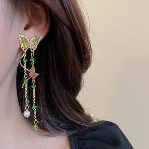 Close-up of long gold earrings with green butterflies and a white pearl on a model