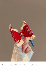 Détail d'une pince à cheveux contrastée rouge et crème tenue à la main pour le style
