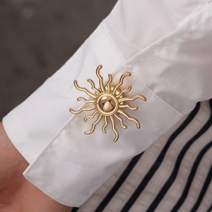 Close-up of golden sunflower cufflink on white shirt sleeve with premium metallic finish