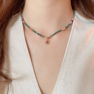 Détail du collier de perles avec pierres vertes et pendentif soleil doré et gemme rose