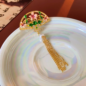 Macro detail of fan brooch with enamel pink floral patterns and a pearl tassel drop