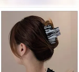 Detail view of large ink-patterned acetate hair claw clip worn on long wavy hair