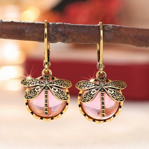 Detail von Vintage Libellen Ohrringen mit rosa Perlen an einem rustikalen Holzzweig