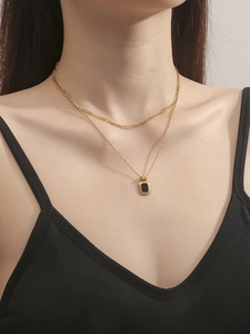 Close-up of double-layered gold necklace featuring a black rectangular pendant on model