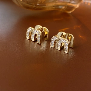 Macro shot of gold-plated 'm' letter earrings with sparkling cubic zirconia on leather
