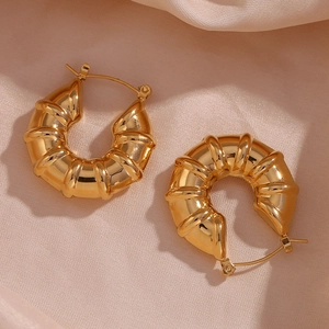 Detailed macro view of 18K gold-plated chunky ribbed hoop earrings on pink silk fabric