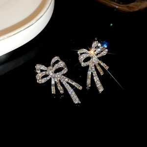 Macro shot of sparkling crystal bow-shaped silver stud earrings on a dark reflective surface