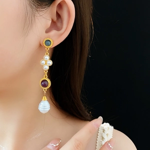 Close-up of vintage gold earrings with dark gems and baroque pearls on a model